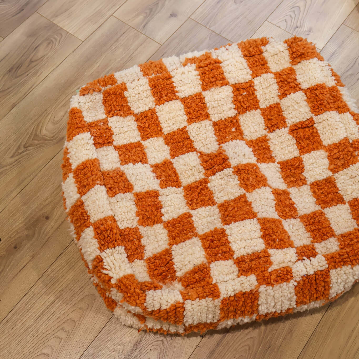 pouf Beni Ouarain damier orange sur un parquet en bois