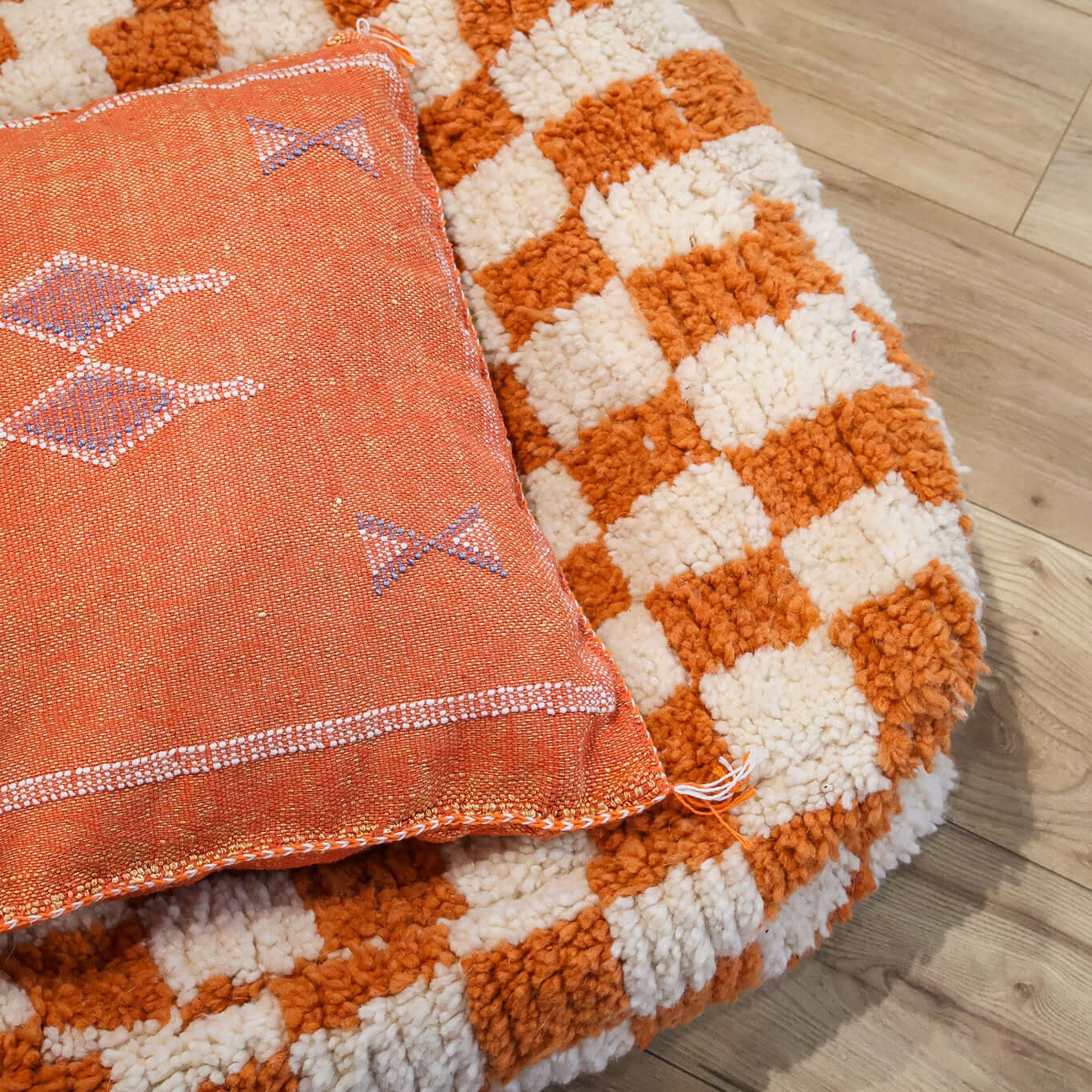 pouf Beni Ouarain damier orange sur un parquet en bois