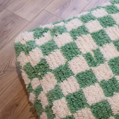 pouf Beni Ouarain damier vert menthe sur un sol en bois clair, mettant en avant son design graphique et artisanal.