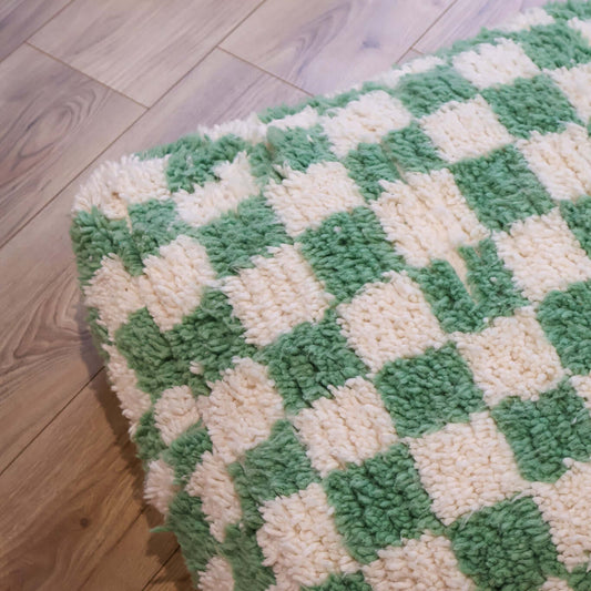 pouf Beni Ouarain damier vert menthe sur un sol en bois clair, mettant en avant son design graphique et artisanal.